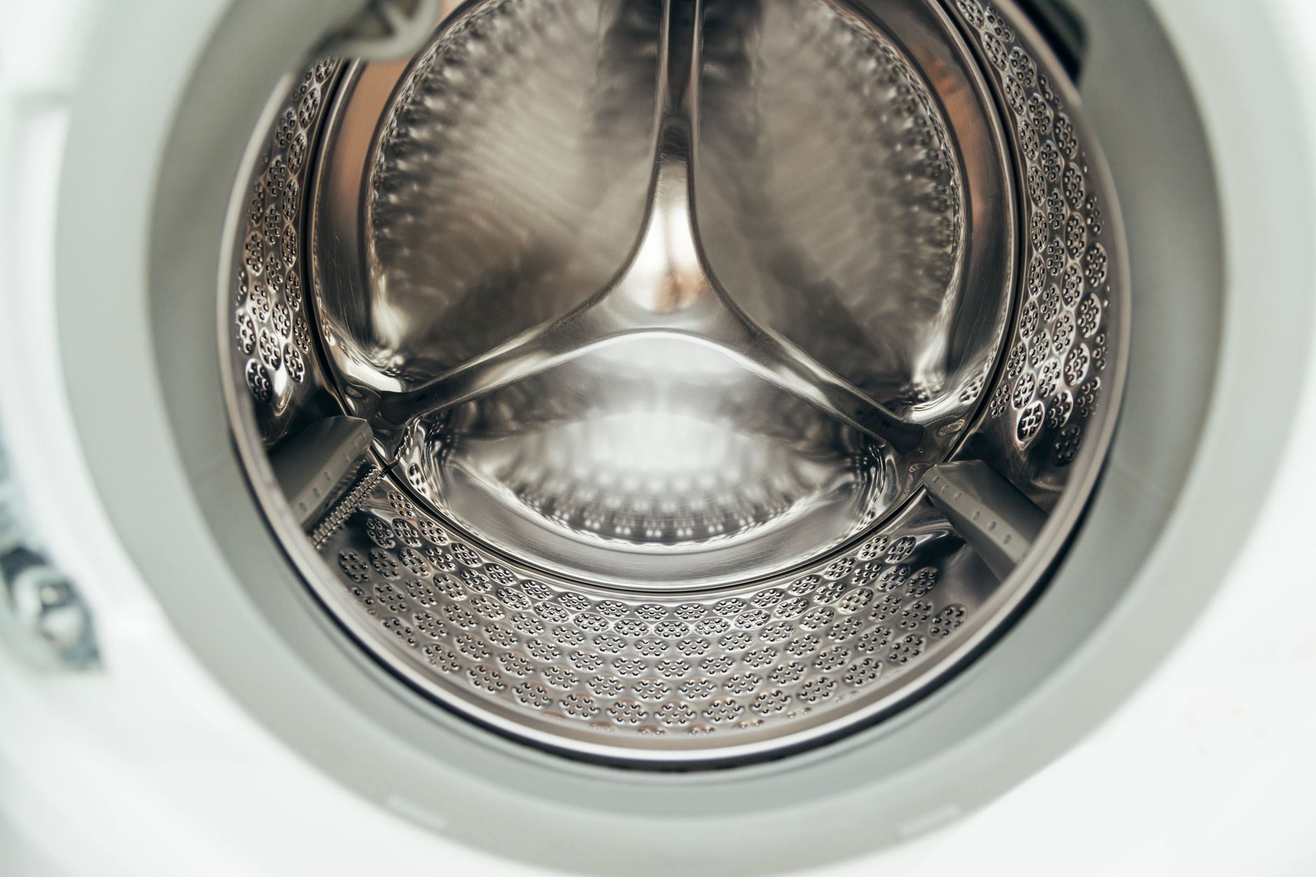a hand pouring white laundry detergent powder into a washing machine drum