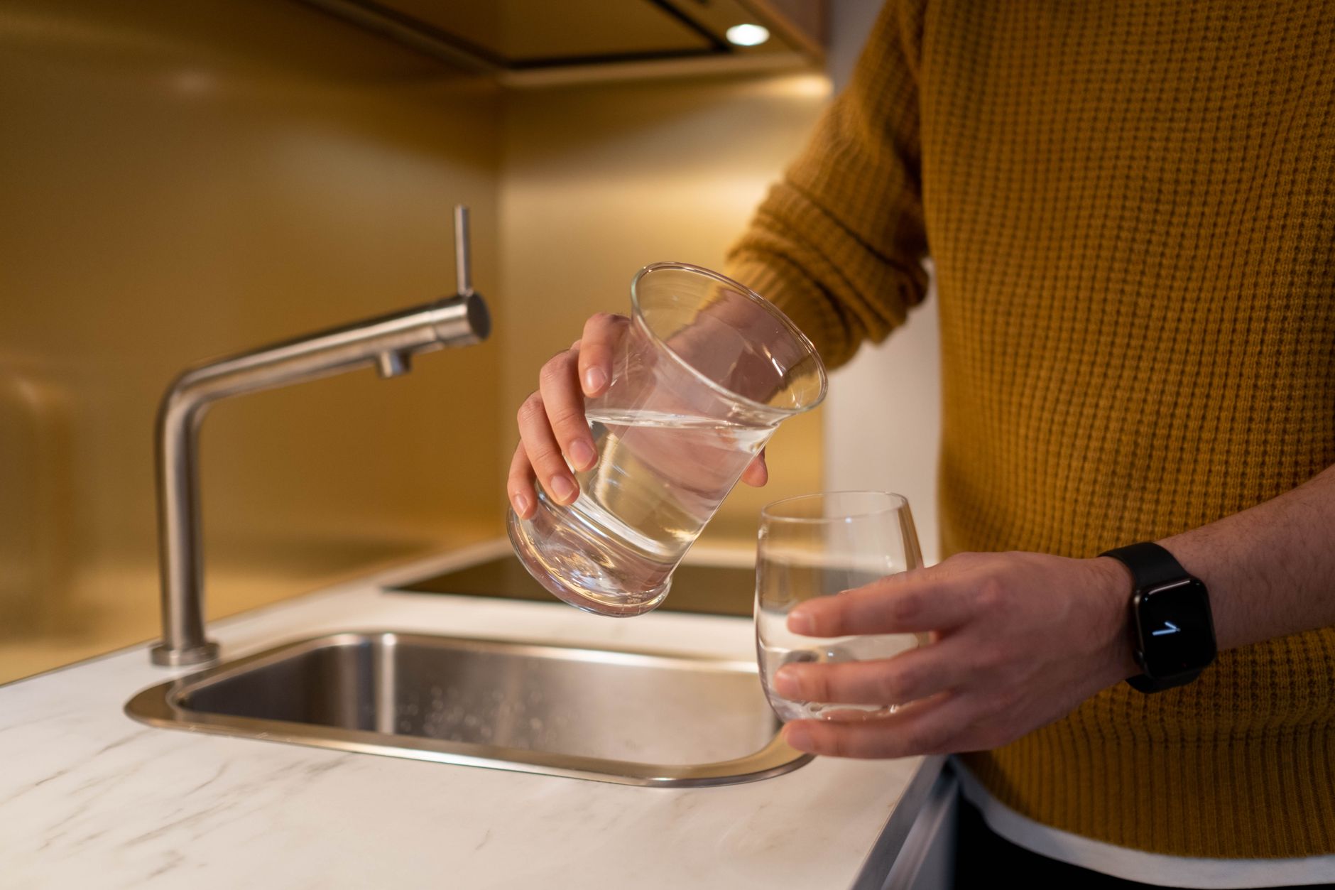A water filter pitcher filling a glass on a kitchen counter